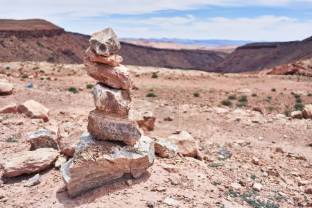 Photo for A balanced stack of stones stands in the forefront of a vast, arid desert landscape under a clear blue sky. - Royalty Free Image