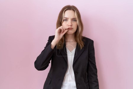 Young caucasian business woman wearing black jacket mouth and lips shut as zip with fingers. secret and silent, taboo talking 
