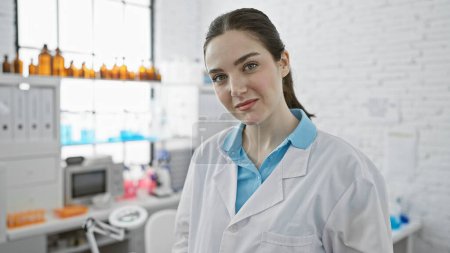 Foto de Retrato de una joven confiada en bata de laboratorio blanca en un laboratorio médico brillante en el interior. - Imagen libre de derechos