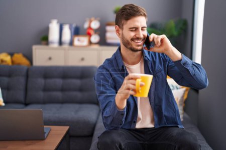 Téléchargez les photos : Young caucasian man talking on smartphone drinking coffee at home - en image libre de droit