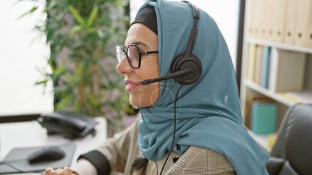 Téléchargez les photos : Une femme professionnelle portant un hijab et un casque travaillant dans un environnement de bureau moderne. - en image libre de droit