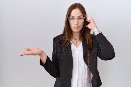 Photo for Beautiful brunette woman wearing business jacket and glasses confused and annoyed with open palm showing copy space and pointing finger to forehead. think about it. - Royalty Free Image