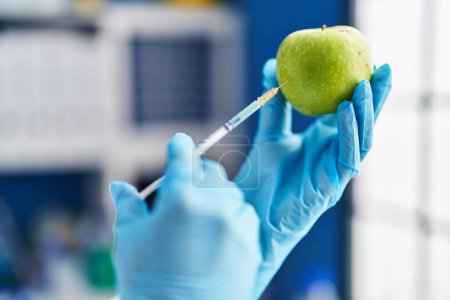 Téléchargez les photos : Femme d'âge moyen scientifique injectant du liquide sur la pomme au laboratoire - en image libre de droit