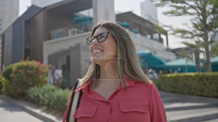 Foto de Una joven hispana adulta sonriente con cabello moreno usando gafas en un entorno deportivo de la ciudad de dubai. - Imagen libre de derechos