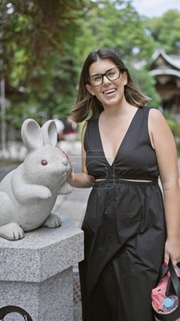 Photo for Happy portrait of a beautiful hispanic woman in glasses, cheerfully standing by a cute bunny rabbit statue at the ancient okazaki jinja temple, embodying japanese culture and tradition in kyoto - Royalty Free Image
