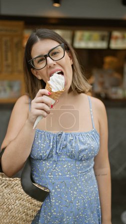Téléchargez les photos : Joyeux hispanique femme savoure délicieusement douce crème glacée sur kyoto rue, son beau sourire est encadré par des lunettes tout en faisant l'expérience de l'architecture traditionnelle de cette ville japonaise - en image libre de droit