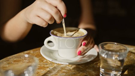 Close-up of a woman stirring coffee in a cozy cafe setting, capturing a relaxed indoor moment.