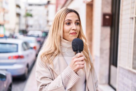 Foto de Mujer joven rubia reportera que trabaja usando micrófono en la calle - Imagen libre de derechos