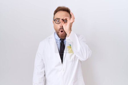 Photo for Middle age doctor man with beard wearing white coat doing ok gesture shocked with surprised face, eye looking through fingers. unbelieving expression. - Royalty Free Image