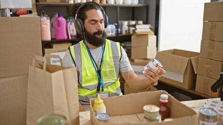 Photo for Hispanic man with headphones in safety vest inspecting goods at warehouse. - Royalty Free Image