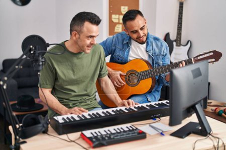 Téléchargez les photos : Two men musicians playing piano and classical guitar at music studio - en image libre de droit