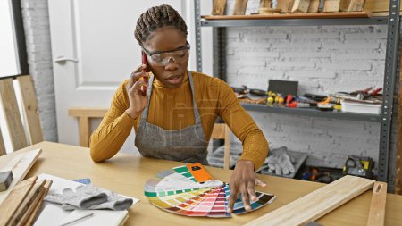 Téléchargez les photos : Femme afro-américaine dans un atelier parlant au téléphone tout en sélectionnant des couleurs de peinture à partir d'un échantillon. - en image libre de droit