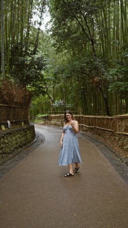 Téléchargez les photos : Se sentant joyeuse, confiante et insouciante, une belle femme hispanique portant des lunettes sourit en marchant vers la caméra dans la forêt de bambous de Kyoto - en image libre de droit