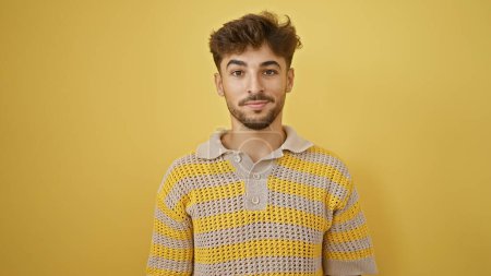 Photo for Stylish young arab man coolly bears his serious expression, standing lone against a stark yellow background. - Royalty Free Image