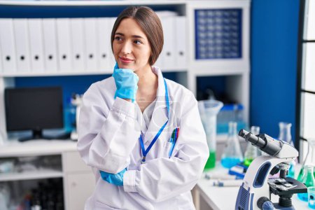 Photo for Young beautiful hispanic woman scientist smiling confident sitting on chair at laboratory - Royalty Free Image