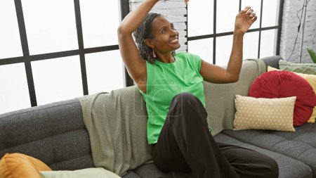 Téléchargez les photos : Femme afro-américaine s'étirant joyeusement dans un salon confortable - en image libre de droit