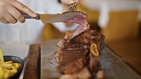 Téléchargez les photos : Jeune femme coupant des tranches de steak de bœuf au restaurant - en image libre de droit