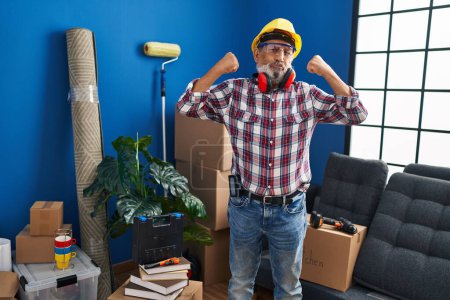 Photo for Confident senior man flexes his muscles, rocking hardhat and safety glasses in his new home, a powerful concept of fitness and strength! - Royalty Free Image