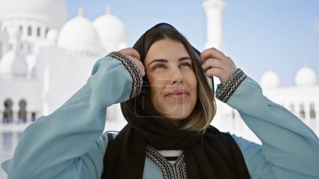 Foto de Una joven sonriente con un hiyab posa frente a la gran mezquita de Sheikzayed en abu dhabi. - Imagen libre de derechos