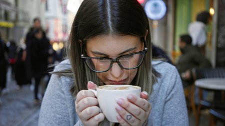 Téléchargez les photos : Une jeune femme portant des lunettes profite d'une tasse de café sur une terrasse extérieure entourée d'activités urbaines. - en image libre de droit