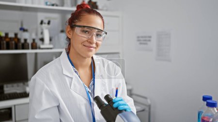 Photo for Radiant young redhead woman scientist smiling while performing biolological analysis with microscope in the heart of a high-tech lab - Royalty Free Image