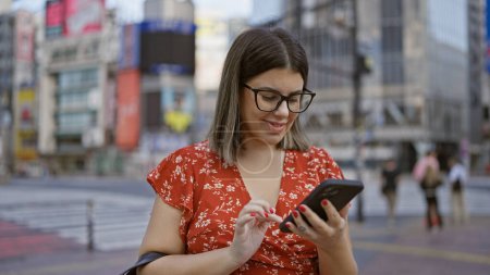 Photo for Smiling beautiful hispanic woman in glasses uses phone on bustling tokyo street, enjoying modern city's vibe, cheerfully texting away - Royalty Free Image
