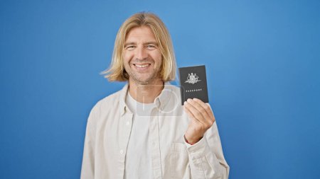 Foto de Hombre rubio sonriendo sosteniendo pasaporte australiano aislado sobre fondo azul - Imagen libre de derechos