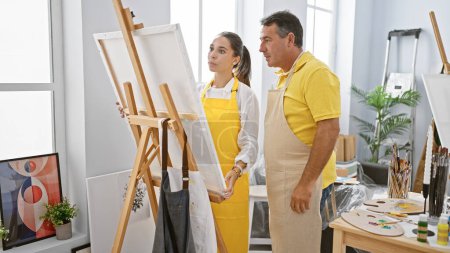 Photo for In an art studio, a man and woman artists decked in aprons, intently looking at the drawing they've created together - Royalty Free Image