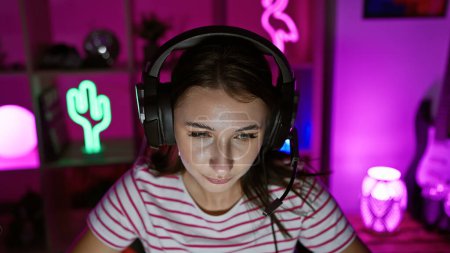 Téléchargez les photos : Une jeune femme concentrée portant un casque dans une salle de jeux dynamique à la maison la nuit. - en image libre de droit