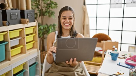 Photo for Young beautiful hispanic woman artist smiling confident using laptop at art studio - Royalty Free Image