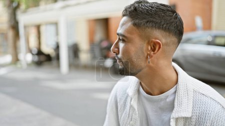 Téléchargez les photos : Beau jeune homme adulte avec une barbe pose dans une rue de la ville, respirant la confiance et le style dans un cadre urbain. - en image libre de droit