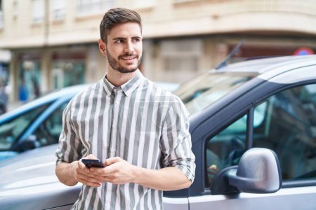 Photo for Young caucasian man using smartphone leaning on car at street - Royalty Free Image