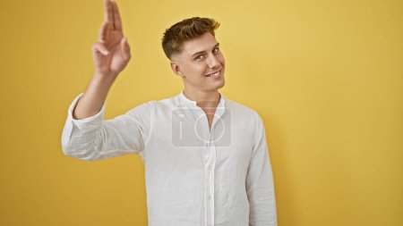 Photo for Joyful and confident caucasian man saluting with his fingers, smiling brightly against an isolated yellow background - Royalty Free Image
