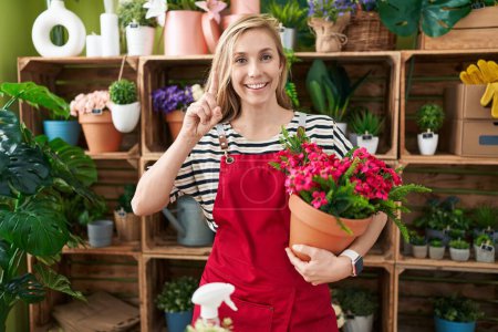 Téléchargez les photos : Jeune femme caucasienne travaillant au magasin de fleuriste tenant l'usine surprise avec une idée ou une question pointant du doigt avec le visage heureux, numéro un - en image libre de droit