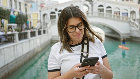 Photo for A smiling brunette woman in glasses uses a smartphone by venetian-style water channels in las vegas. - Royalty Free Image