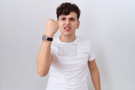 Téléchargez les photos : Jeune homme non binaire portant un t-shirt blanc décontracté en colère et fou levant le poing frustré et furieux tout en criant de colère. rage et concept agressif. - en image libre de droit