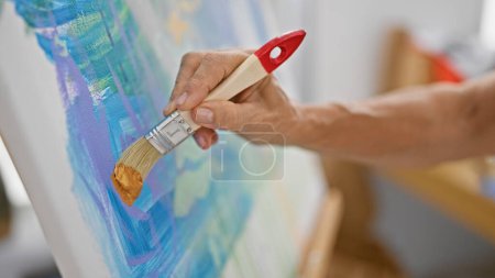Téléchargez les photos : Gros plan d'une peinture à la main avec un pinceau large sur une toile colorée dans un cadre d'atelier d'art. - en image libre de droit