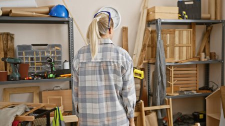 Photo for Back view of a young woman in safety glasses standing in a carpentry workshop - Royalty Free Image