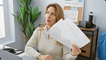 Photo for A thoughtful hispanic woman examines documents in a modern office, evoking professionalism and concentration. - Royalty Free Image