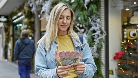 Téléchargez les photos : Jeune femme blonde comptant le zèle et les dollars dans une rue de la ville, incarnant le voyage, la finance et la vie urbaine. - en image libre de droit