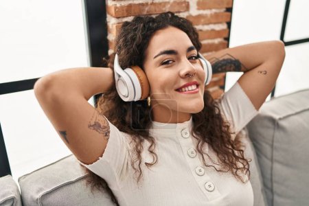 Téléchargez les photos : Jeune belle femme hispanique écoutant de la musique assise sur le canapé à la maison - en image libre de droit