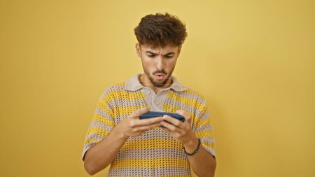 Foto de Hombre árabe joven jugando videojuego por teléfono inteligente sobre fondo amarillo aislado - Imagen libre de derechos