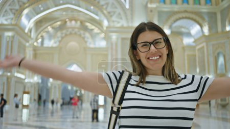 A smiling woman with glasses takes a selfie in the grand interior of qasr al watan in abu dhabi. Poster 703145752
