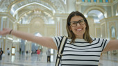 A smiling woman with glasses takes a selfie in the grand interior of qasr al watan in abu dhabi. Poster #703145752