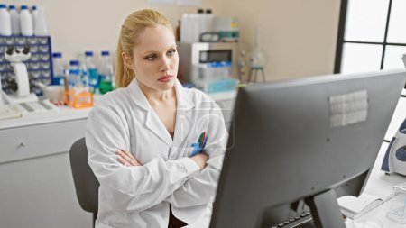 Foto de Mujer rubia enfocada en bata de laboratorio analiza los datos de la computadora en el laboratorio moderno. - Imagen libre de derechos