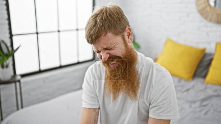 Photo for Handsome irish redhead adult man, stressed and suffering, sitting in bed early morning, indoor apartment bedroom, concentrating on his problems - Royalty Free Image