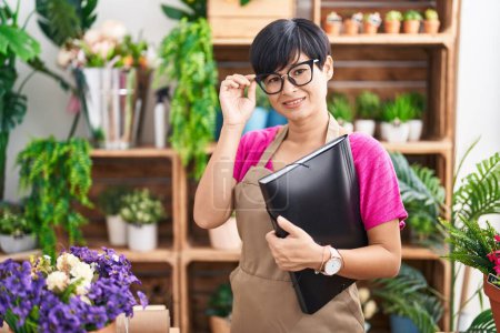 Photo for Middle age chinese woman florist smiling confident holding binder at flower shop - Royalty Free Image