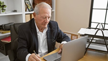 Téléchargez les photos : Portrait d'un homme âgé concentré, un travailleur d'affaires mature, assis à son bureau, profondément absorbé dans le travail sur son ordinateur portable. cet aîné, patron élégant respire le professionnalisme. - en image libre de droit