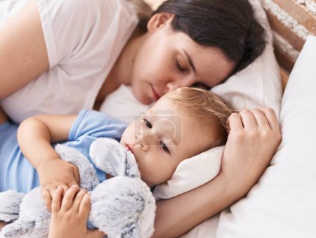 Téléchargez les photos : Mère et fils dormant sur le lit embrassant poupée dans la chambre - en image libre de droit