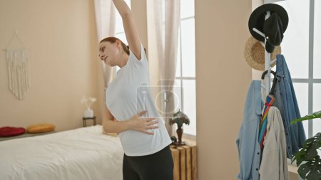 Photo for A young woman stretches in a bright bedroom, adding vitality to a routine morning at home. - Royalty Free Image